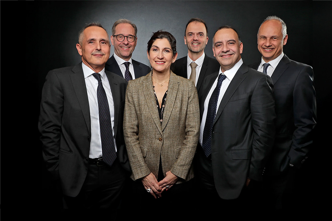 Group portrait of six professionals in business attire against a dark background.
