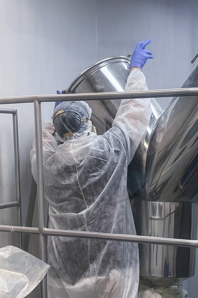 Person in protective gear handling a large metal container in a clean environment.