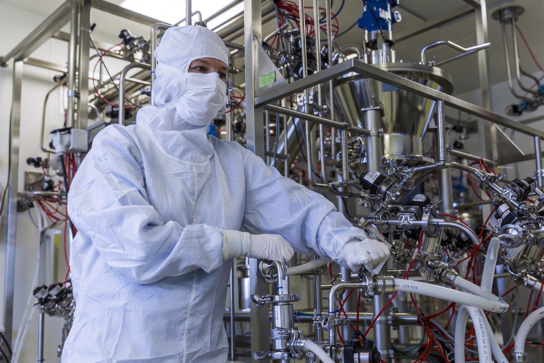 Worker in protective gear operating machinery in a pharmaceutical factory.