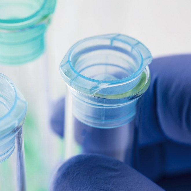 Close-up of test tubes with blue caps held by a gloved hand