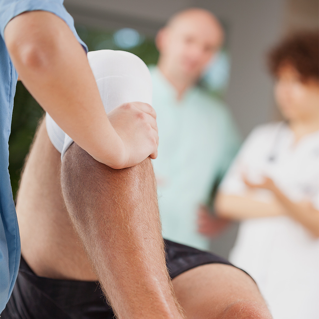 Person with a bandaged knee being examined by two medical professionals.