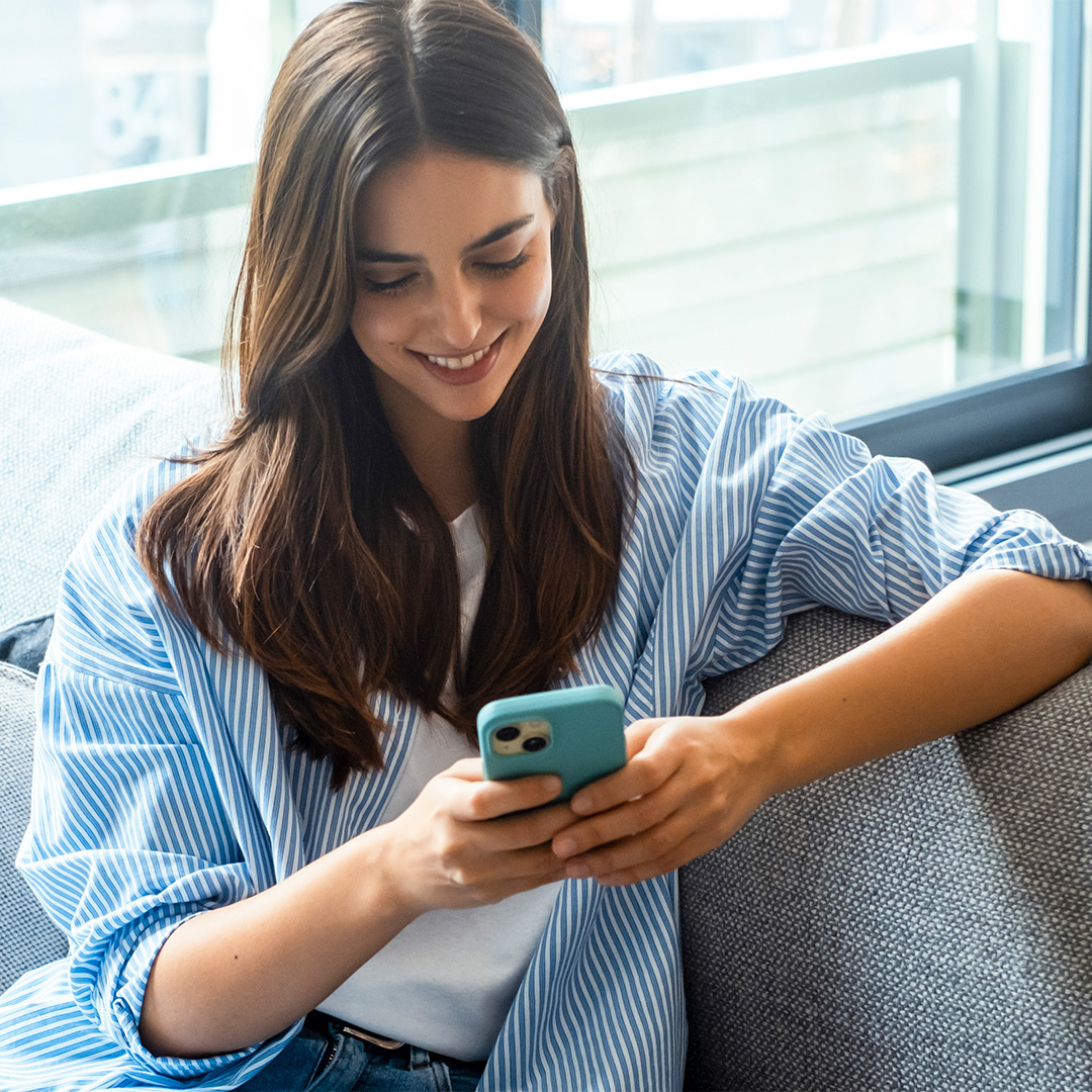 Young woman smiling while using a smartphone on a sofa