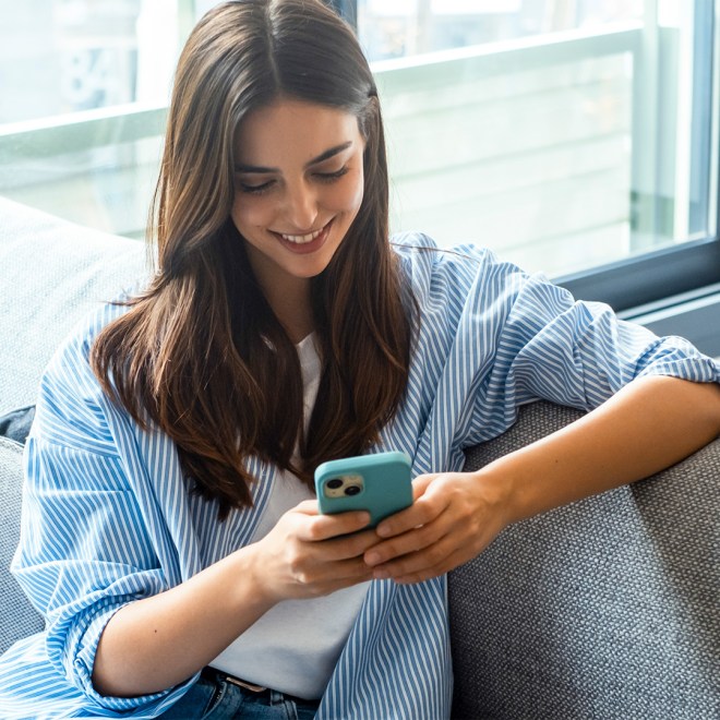 Young woman smiling while using a smartphone on a sofa