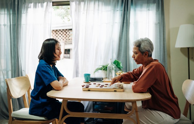 A young woman and an older woman playing a board game at a table.