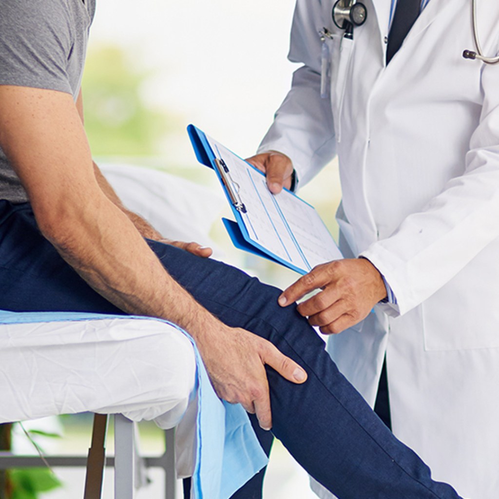Doctor examining a patient's leg while holding a clipboard